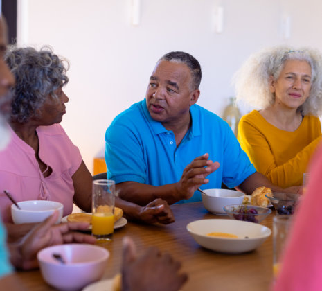 senior friends talking and eating healthy breakfast at dining table in nursing home